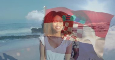 Kadın direği tutuyor, erkek yaklaşıyor, sarılıyor ve sevgisini gösteriyor. Seyahat reklamı için hareketli bayrak kaplıyor. Plaj, çift, romantizm, damalı, dalgalar, güneş ışığı, deniz kenarı