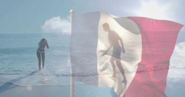 Kadın geri çekilirken dalga yaklaşıyor. Adam bayrağın arkasında tepiniyor. Boş zamanlarını gösteren bir seyahat reklamı. Plaj, çift, güneşli, dalgalar, bayrak, hareket, mercek