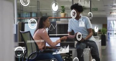 Kadın dizüstü bilgisayara işaret ederken, erkek AR tabletinin çizelgeleriyle yaklaşıyor iş kararına rehberlik ediyor. İşbirliği, iş arkadaşları, ofis, gösterge panelleri, grafikler, teknoloji, üretkenlik