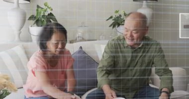 Çift kupaya uzanıyor, ev teknolojisiyle kahve servisi yapıyor ve İHD şebekesi çiftleri örtüyor. Salon, kanepe, minimalist, modern, iç mekan, rahat, bitkiler.