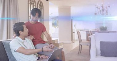 Oturmuş bir adam dizüstü bilgisayarda dizüstü bilgisayar başında oturmuş, öne eğiliyor, teknolojik içeriği paylaşıyor ve gülümsüyor. Aile, ev, işbirliği, teknoloji, ekran, oturma odası, günlük