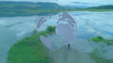 Kadın kıyıda duruyor, dünya tepesinde süzülüyor, kıtaları teknoloji için gösteriyor. Hava, dron, yarımada, göl, yansıma, manzara, tefekkür