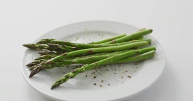 Masadaki beyaz tabakta biberle paralel duran yeşil kuşkonmaz mızraklarını gösteriyor. Verdant, Prodüksiyon, Tazelik, Makro, Minimalist, Stüdyo, Mutfak