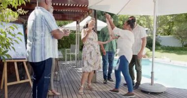 Çiçekli elbiseli bir kadın güvertede dans ediyor, konuklar kuşağı etkinliğe göre ayarlıyor. Arka bahçe, havuz kenarı, pergola, balonlar, saç bandı, sehpa, açık hava.