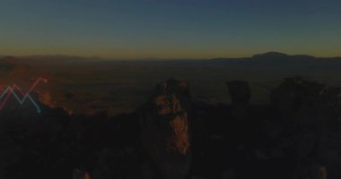 Güneş doğuyor, hava kamerası geri çekiliyor ve dönüyor, neon çizgileri çizerken vadiyi ortaya çıkarıyor. Ek, mesa, kanyon, çöl, drone, panorama, ufuk