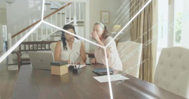 İki kadın dizüstü bilgisayara yaslanmış, akıllı telefon gösteren, teknolojik verileri gözden geçiren iki kadınla. İşbirliği, takım çalışması, tablet, senaryo paylaşımı, holografik, geometrik, gün ışığı