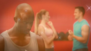 Başroldeki adam pano notlarını bitiriyor, yukarı bakıyor ve jimnastik salonunda kıvılcımlar saçarak kamerayı selamlıyor. Ağırlıklar, stüdyo, fitness, antrenör, üçlü, odaklanma, samimiyet