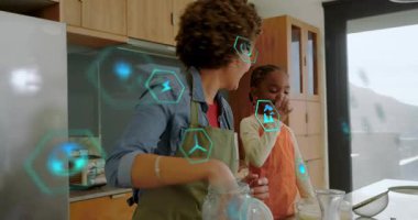 Anne ve kızı kaşık tadıyorlar sonra da pişirmek için yumurta kırıyorlar, teknoloji altıgenleri yüzüyor. Aile, mutfak, bağlanma, öğrenme, rehberlik, çocuk, aşçılık