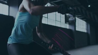 Savaş halatlarını çeken bir kadın, spor salonunda güç için dalgalara çarpan bir kadın, hareket eden mor çizgiler. Halatlar, fitness, antrenman, atlet, depo, arka ışıklandırma, eldivenler