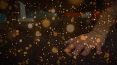 Adam sağ elini masaya koyuyor, parmaklarını oynatıyor altın bokeh sürüklenirken, teknolojiyi gizliyor. Kol, yüzey, bileklik, siluet, parçacık, ışıltı, sıcak