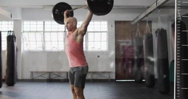 Erkek kaldırıcı kafasının üstünde çubuk tutuyor, sabitliyor ve formda kalmak için çömeliyor. Halter, spor salonu, güç, antrenman, atletik, odaklanma, güneş ışığı