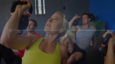 Kadın ve grup elektrokardiyogramda ağırlık kaldırıyor. Kolları kafasının üstünden zinde. Ağırlıklar, stüdyo, spor salonu, egzersiz, senkron, hareket, nabız