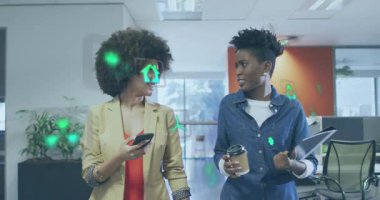 İki kadın koridorda yürüyor, bakışlarını paylaşıyor ve iş yeşil simgelerinden bahsederken telefon okuyor. Meslektaşlar, ofis, koridor, açılış planı, sohbet, kahve, tablet