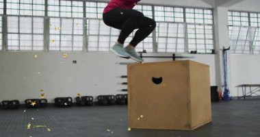 Çeyrek çömelme ve kol sallama yapan bir kadın, fitness için pyo kutusunda patlıyor, altın yıldızlarla kaplanıyor. Plyometrik, atlama, güç, güç, spor salonu, antrenman, güneş ışığı