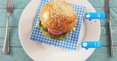 İlk mavi baloncuk ortaya çıkıyor, mavi baloncuklar susamlı burgerin yanında çoğalıyor, artan beğeni gösteriyor. Düz döşeme, genel giderler, masa üstü, çörek, tabak, peçete.