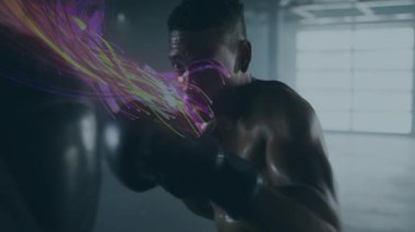 Boksör yumruklamaya başlıyor, kombinasyonlar atıyor, hareket yollarını gösteriyor eldiven bağlıyor ve ağır torba eğitimi alıyor. Dövüşçü, spor salonu, arka ışıklandırma, karamsar, fitness, yoğunluk, odaklanma