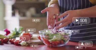 Aşçı soğanı cam kaseye boşaltıyor, yemek promosyonu için salatayı ellerin etrafında yüzen ikonlarla karıştırıyor. Önlük, mutfak, marul, domates, tezgah, kesme tahtası, canlı