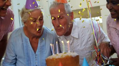 Dört son sınıf öğrencisi evde doğum günü pastasının etrafında eğilip mum soluyor ve konfeti yolluyor. Kutlama, toplanma, şenlik, sevinç, sıcaklık, güneş ışığı, iç mekan