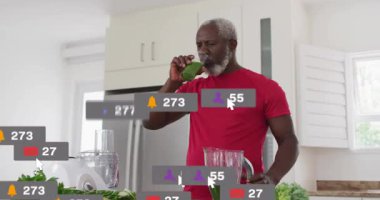 Olgun bir adam, sosyal bildirimler artarken tezgah paylaşım tarifinde yeşil içeceği yudumluyor. Mutfak, smoothie, blender, sağlıklı, yaşam tarzı, gün ışığı, modern