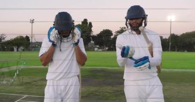 İki vurucu dirseklerini vuruyor, kriket sahasını terk ediyor, çizelgeleri yerleştirirken kaskları çıkarıyor. İkili, saha, alacakaranlık, projektörler, eldivenler, başlıklar, yarasa