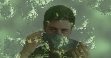 Yetişkin erkek, yeşil parçacıklar yüzün üzerinde hareket ederken gri sağlık maskesi kaldırma döngülerini kontrol ediyor. Stüdyo, portre, yakın çekim, yalnız, sakin, yumuşak, aydınlatma