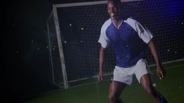 Erkek futbolcu kaleye hazırlanıyor, topla buluşuyor, kafasının üstünde canlı bir işaret fişeğiyle ilerliyor. Defans, açık hava, gece, çim, projektör, atletik, hareket