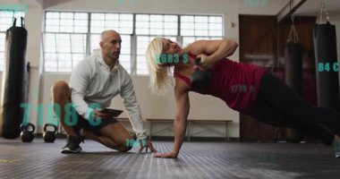 Eğitmen işaret veriyor, kadın çekirdek basıncını arttırmak için kettlebell yan tahtası yapıyor, ölçüler üst üste biniyor. Spor salonu, fitness, antrenman, ağırlık, koçluk, stüdyo, denge