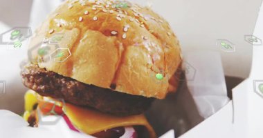 Kamera kayması, paket servis hamburgeri ortaya çıkartırken yeşil büyüyen uğursuzluklar malzemelerin altını çiziyor. Sandviç, ambalaj, paket, fast food, parlak, peynir.