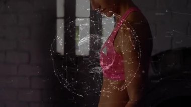 Aşağı bakan, uzanan ve halterini kıvıran bir kadın, göğsünde dönen baygın bir küre. Ağırlıklar, antrenmanlar, güç, spor salonu, stüdyo, arka ışıklandırma, tuğla