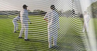 Dört erkek oyuncu spor sahasında içe doğru hareket ediyor, bir tanesi nesne seçmek için eğiliyor, sağa doğru dalgalanıyor. Açık hava, çimen, birlik, takım çalışması, atletik, şapkalar, gölgeler