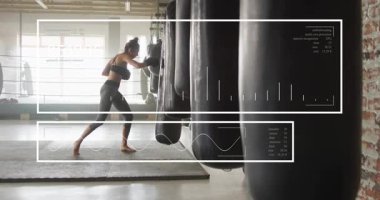 Dişi boksör öne çıkıyor, ağır torbalara yumruk ve haç atıyor, HUD ölçümleri gösteriyor. Spor salonu, boks, yalınayak, antrenman, spor, kardiyo, stüdyo