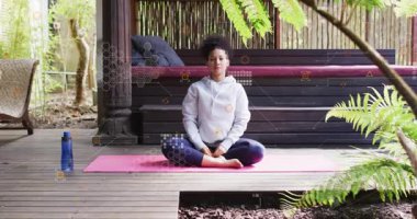 Kadın nefes alıyor ve pembe paspasın üzerinde yan yana oturmaya başlıyor. İşaretleme formunu kaplıyor. Yoga, farkındalık, poz, uzatma, genel giderler, veranda, açık hava