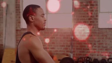 Ağırlık antrenmanı yapan bir adam kolunu kaldırarak kamerayı indirirken, kırmızı bokeh de onu örtüyor. Dumbbell, fitness, muscular, stüdyo, endüstriyel tuğla duvar, odaklanma