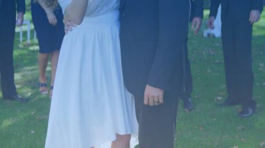 Gelinlik çifti dışarıda düz tasarım içinde duruyor, gelinlik ve siyah takım elbiseli düğün temasını gösteriyorlar. Romantizm, kutlama, zarafet, dinginlik, doğa, neşe, olay