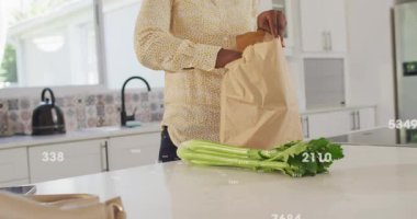 Kadın çantasını açıyor, yakınlarda kereviz var, havuçlara uzanıyor, paketleri açıyor, sayısal UI sayılarını gösteriyor. Mutfak, üretim, sebze, ada, tezgah, gün ışığı, modern