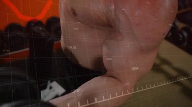 Dambıl tutan erkek stajyer, kıvırcık saçlı, hareketli kırmızı çizelge, spor salonundaki temsilcileri takip ediyor, uzaklaşıyor. Fitness, antrenman, güç, kas, ter, halter, analitik