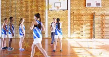 Koç topa vuran kadın atıcı öne çıkıyor. Atış talimi yapıyor. Basketbol, spor salonu, takım çalışması, antrenman, mahkeme, üniformalar, güneş ışığı.