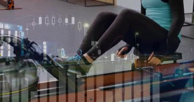 Ayaklarını yerden kesen, kürek çeken, antrenman yapan yarı şeffaf finansal tabloları takip eden bir kadın. Ergometre, kardiyo, atlet, spor salonu, stüdyo, dayanıklılık, odaklanma