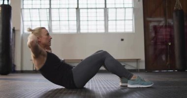 Beden eğitimi yapan kadın mekik çekmeye başlıyor ve arkasına yaslanıyor, gövdesine güç yüklüyor. Çekirdek, karın kası, spor, atletik, stüdyo, endüstriyel