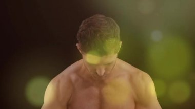 Erkek fitness modeli başıyla eğilirken kamera genişliyor ve parlıyor, kasları göstermek için esniyor. Vücut geliştirici, heykeltraş, fizik, karın kası, kol, göğüs, göğüs kasları.