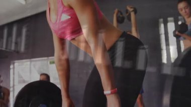 Halter tutan ve spor salonunda menteşe başlatan kadın, güç ölçümlerini takip eden hareketli gövde çizelgeleri. Grup, kettlebell, antrenman, stüdyo, fitness, odak, yoldaşlık