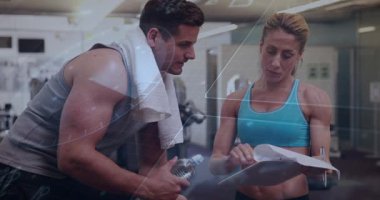 Kadın antrenör panoya işaret ediyor, müvekkil öne eğiliyor, fitness planını onaylıyor, üstüste biniyor. Koç, spor salonu, ekipman, stajyer, havlu, su, danışma