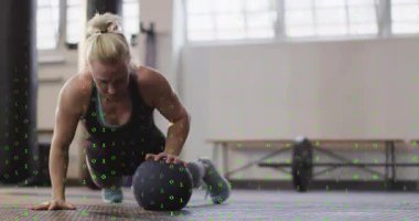 İlaç topundan başlayan bayan sporcu, vücut dengesini sağlamak için tek koluyla şınav çekiyor. Güç, antrenman, spor, stüdyo, halter, denge