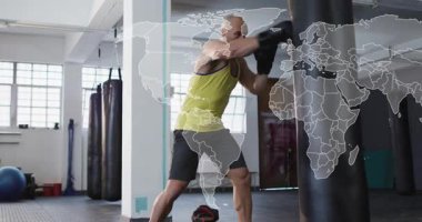 Erkek boksör kayıyor, kum torbası eğitiminde kombinasyon atıyor, dünya haritası kareyi yumruklar inerken örtüyor. Boks, spor salonu, gün ışığı, odaklanma, atletik, güç, dayanıklılık