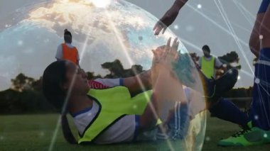 Neon, futbol sahasında bacağını tutuyor, turuncu uzanıyor ve sayı göstererek dünya çapında oynamaya devam ediyor. Takım çalışması, gün batımı, açık hava, antrenman, yelek, çimen, sporcular