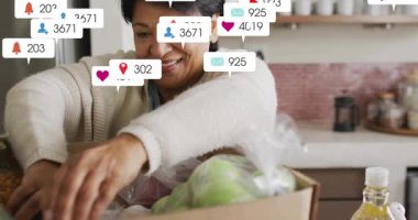 Üst düzey kadın teslimat kutusunu açıyor, sosyal medya rozetleri yüzerken ürünleri düzenliyor. Yaşlılar, ev, mutfak, bakkaliye, meyve, yeşillik, yağ