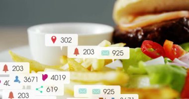 Gelen baloncuklar patlıyor ya da yığılıyor. Sonra hamburger ve patates kızartmaları nişanı gösteriyor. Masa üstü, yakın çekim, düz yatak, sığır eti, çörek, marul, dinamik