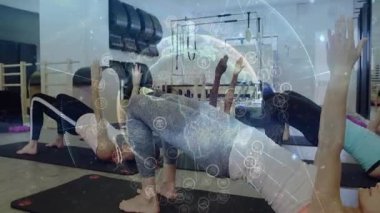 Kadın katılımcılar ders sırasında kalçalarını kaldırıyor, pilates küresi güç için izleme darbelerini örtüyor. Köprü, minderler, stüdyo, fitness, grup, denge, koordinasyon
