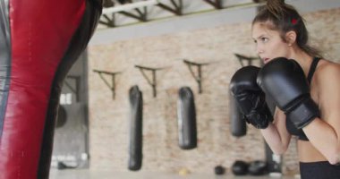 Dişi boksör, gövdesini kaplayan boks antrenmanı için kırmızı çantaya kombinasyon fırlatıyor. Spor salonu, kadın, eldivenler, ağır çanta, tuğla duvar, odaklanma, egzersiz