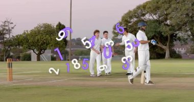 Beş kriket oyuncusu büyük oyundan sonra yürürken, yukarıda mor ve beyaz numaralar dönerken kutlama yapıyorlar. Kriket, takım çalışması, kutlama, açık hava, park, zift, alacakaranlık